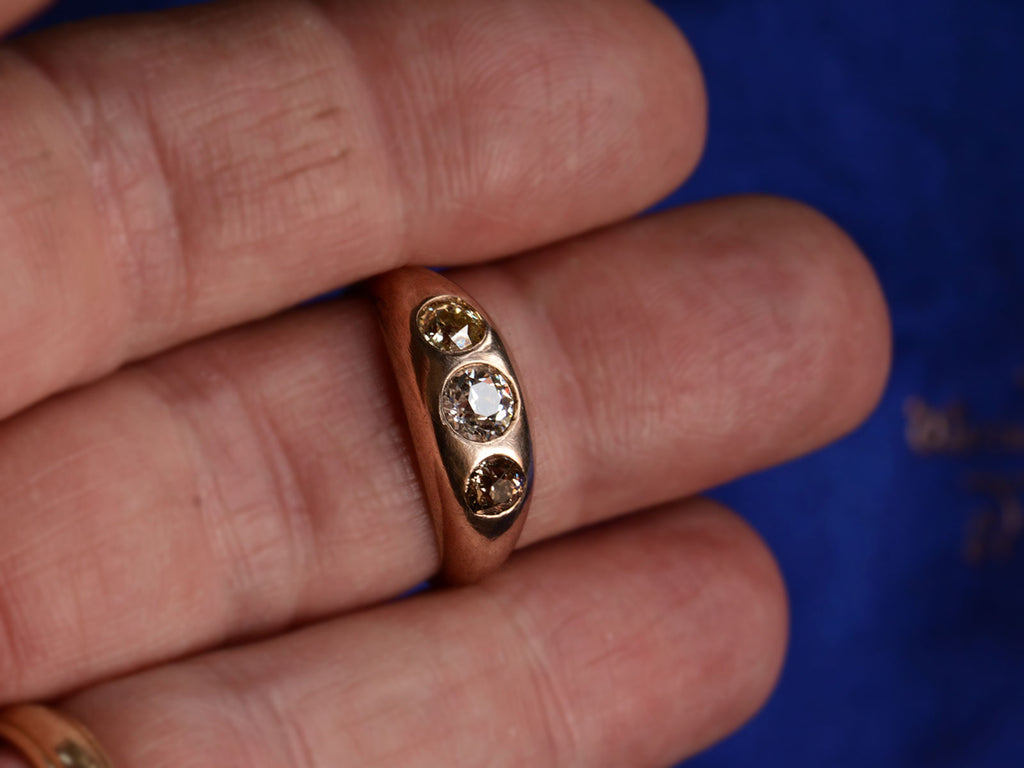 c1890 Victorian Gypsy Ring with a white diamond center and a light yellow and brown diamond on either side in rosy 10k mounting. Shown on finger for scale.