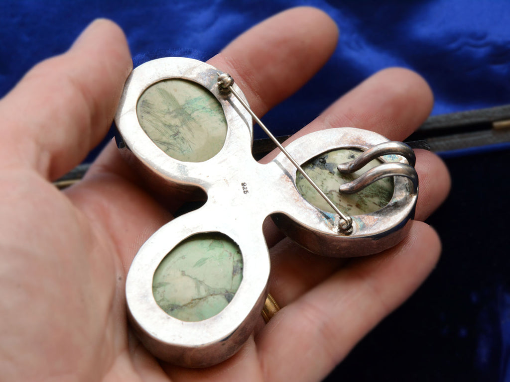 Reverse side of large vintage c19980 brooch with three oval turquoise stones set in silver in a clover-like formation. (Shown on hand for scale). A stamp "925" is visible.