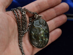 thumbnail of A vintage pendant necklace with labradorite carved with the image of a nude woman, shown on a hand for scale.