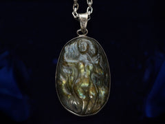 thumbnail of Detail of a vintage pendant necklace with labradorite carved with the image of a nude woman, on a dark background.