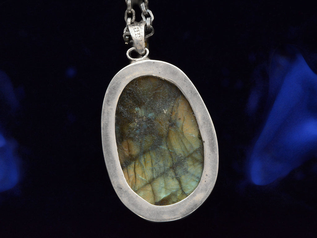 Reverse side of vintage pendant necklace with labradorite carved with the image of a nude woman, on a dark background.