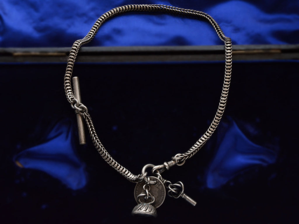 c1880 Victorian silver watch chain with black agate seal fob, a coin, and a watch key, shown on dark background.