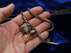 thumbnail of Detail of c1880 Victorian silver watch chain with black agate seal fob, a coin, and a watch key, shown on hand for scale.