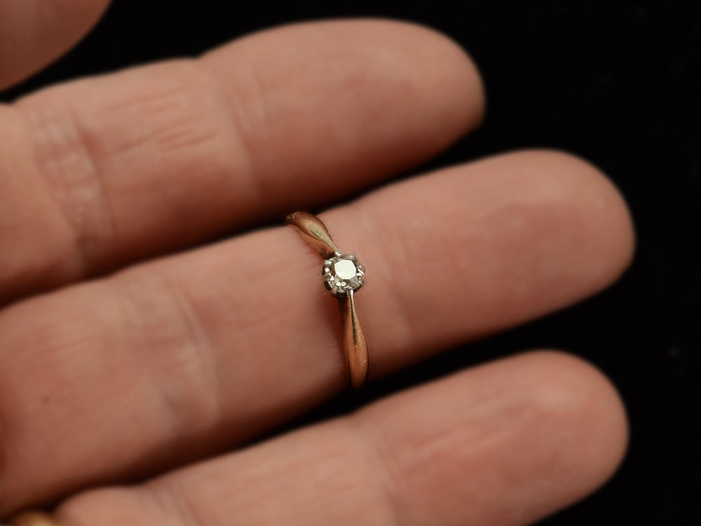 An antique ring with a 0.20ct old mine cut diamond set in a simple silver topped 14K yellow gold mounting, shown on finger.