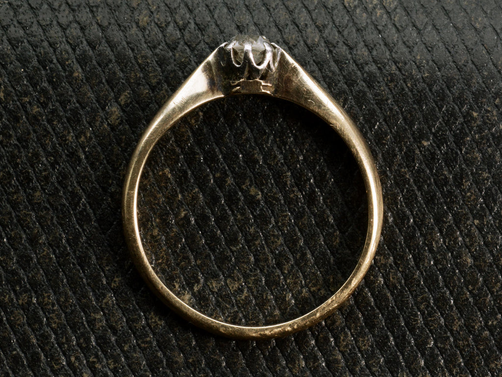 Side profile of an antique ring with a 0.20ct old mine cut diamond set in a simple silver topped 14K yellow gold mounting, shown on dark textured background.