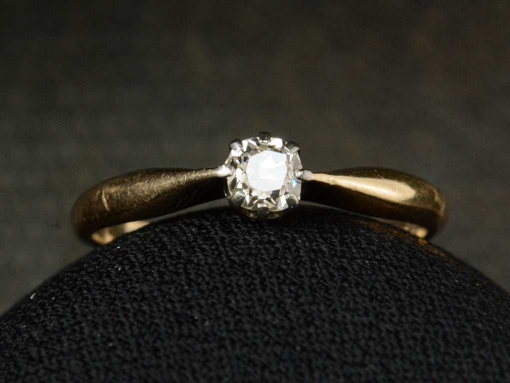 Front view of an antique ring with a 0.20ct old mine cut diamond set in a simple silver topped 14K yellow gold mounting, shown on dark background.