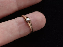 thumbnail of An antique rosy-yellow gold Victorian engagement ring with a small old mine cut diamond in a belcher setting. Shown on finger against dark background