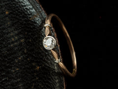 thumbnail of Angled view of an antique Art Deco era yellow and white gold engagement ring with a bezel-set round 0.20ct old European cut diamond. Shown on dark background.