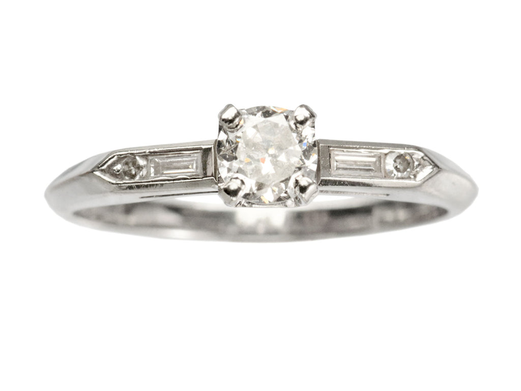 Vintage c1940 white gold engagement ring with small round diamond and rectangular baguettes on either side. Shown on white background.