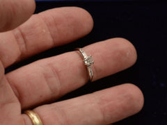 thumbnail of Front view of a vintage c1940 white gold engagement ring with small round diamond and rectangular baguettes on either side. Shown on finger
