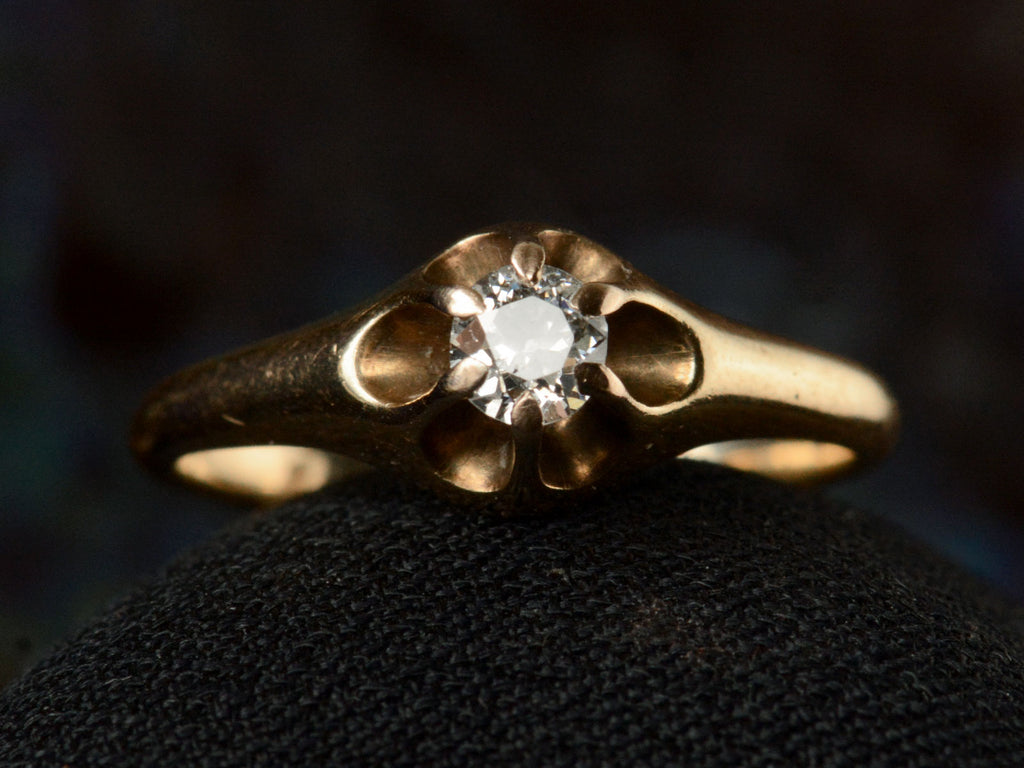Front view of an antique Victorian solitaire engagement ring with a round diamond set in a six pronged rosy-yellow gold belcher mounting. Shown on dark background.