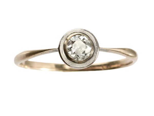 An antique Edwardian era engagement ring with a round diamond in a simple silver topped rosy-yellow gold mounting, shown on white background.