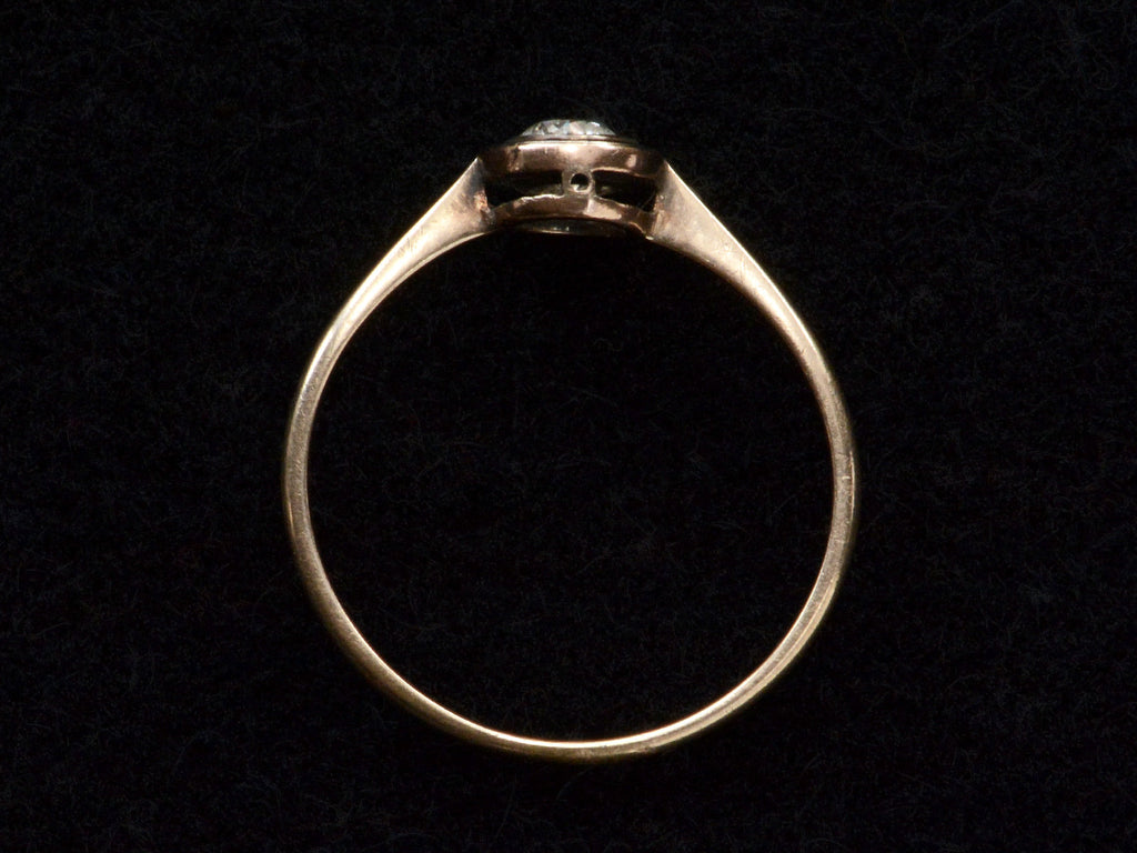 Side profile of an antique Edwardian era engagement ring with a round diamond in a simple silver topped rosy-yellow gold mounting, shown on black background.