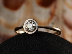 thumbnail of Angled front view of an antique Edwardian era engagement ring with a round diamond in a simple silver topped rosy-yellow gold mounting, shown on dark background.