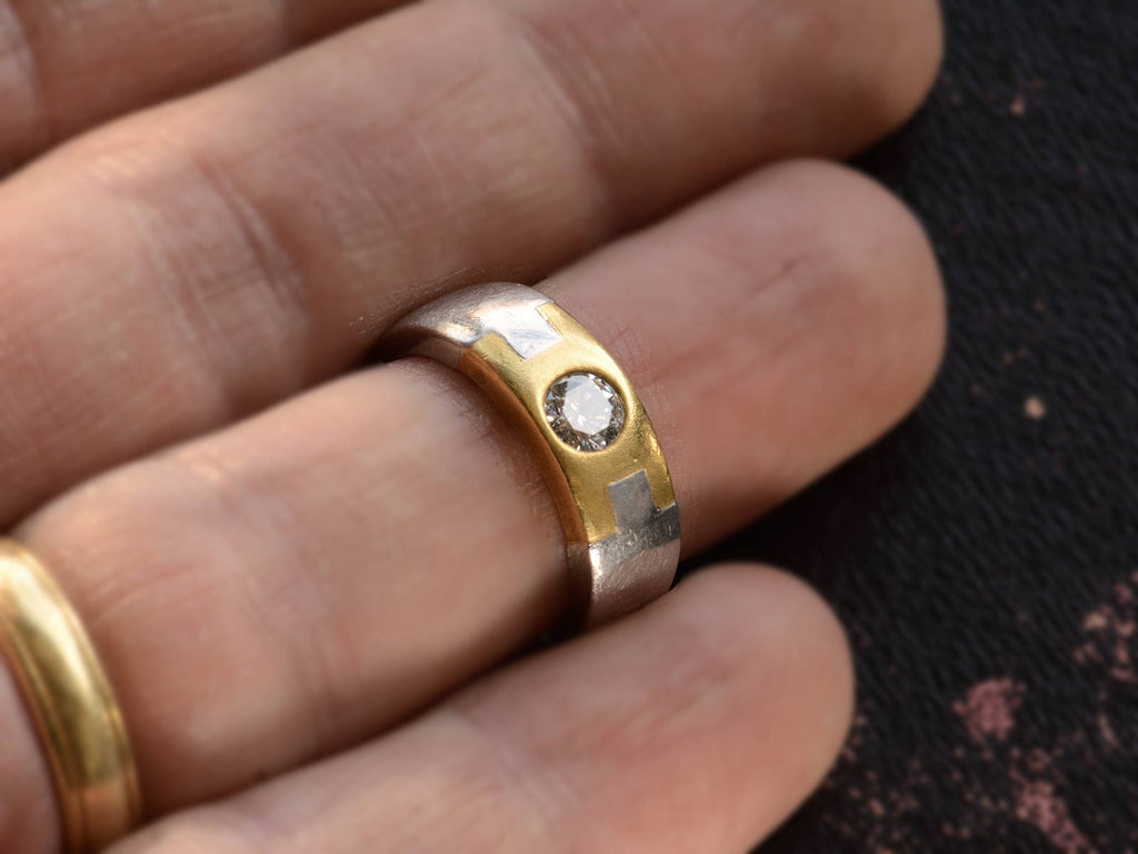 A vintage two toned platinum and yellow gold band set with a round diamond, shown on a finger for scale.