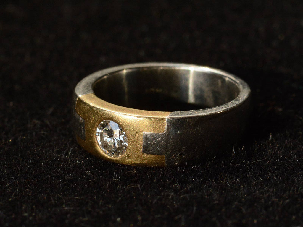 Right angle view of vintage two toned platinum and yellow gold band set with a round diamond, shown on a dark background.