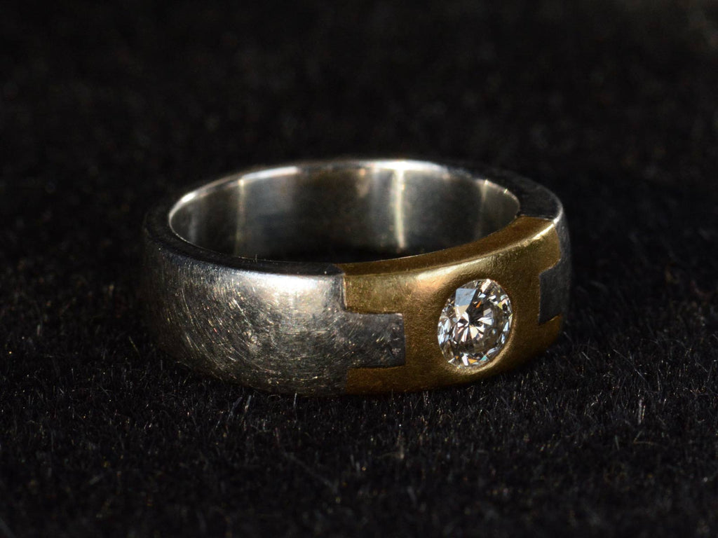 Left angle view of vintage two toned platinum and yellow gold band set with a round diamond, shown on a dark background.