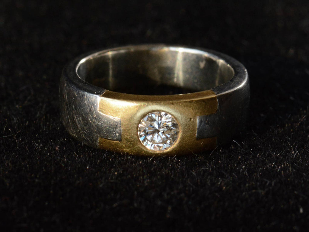 Front view of vintage two toned platinum and yellow gold band set with a round diamond, shown on a dark background.