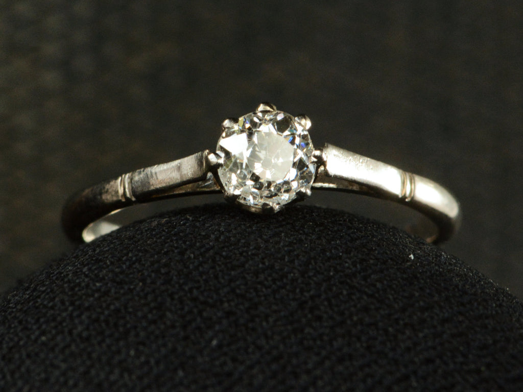 A simple 1920 solitaire engagement ring with a old European cut diamond set in 18K white gold, shown on dark background.