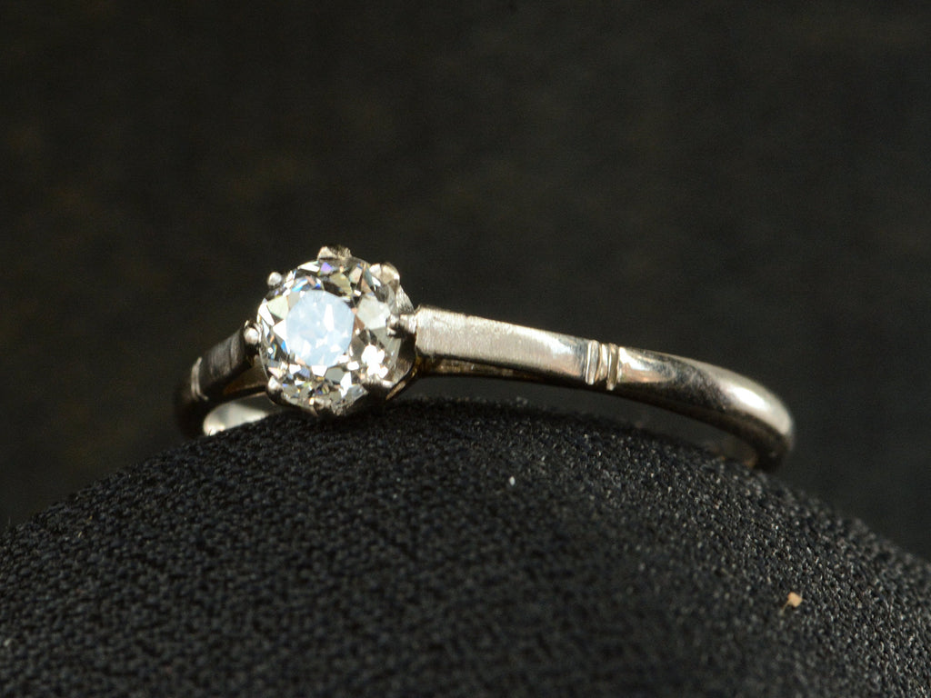 Angled front view of a simple 1920 solitaire engagement ring with a old European cut diamond set in 18K white gold, shown on white background.