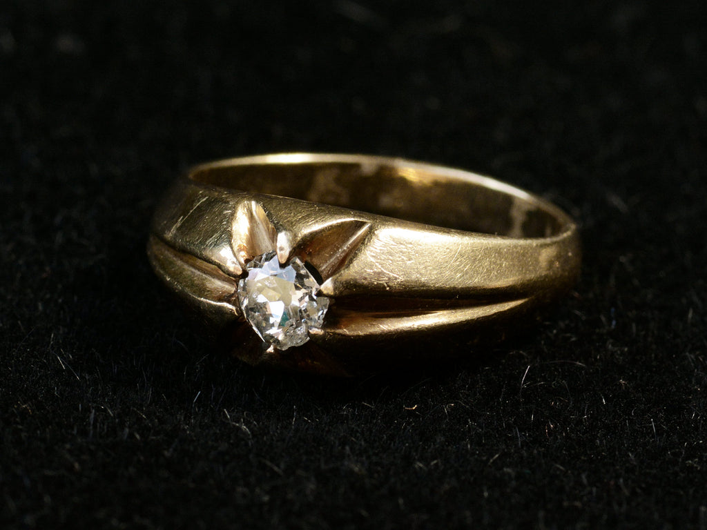 Right angled view of wide antique men's ring with cushion shaped old cut white diamonds set in yellow gold, shown on dark background.