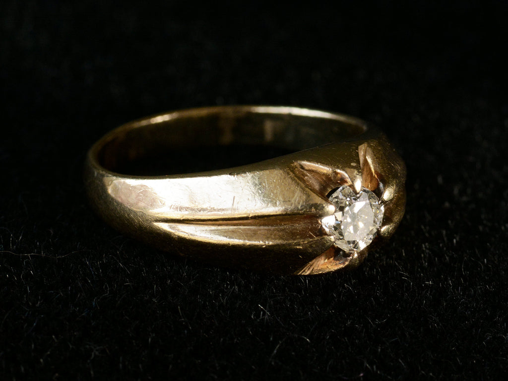 Left angled view of wide antique men's ring with cushion shaped old cut white diamonds set in yellow gold, shown on dark background.