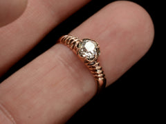 thumbnail of A Victorian solitaire ring with a square old mine cut diamond set in a wide striped rose gold setting, shown on finger.