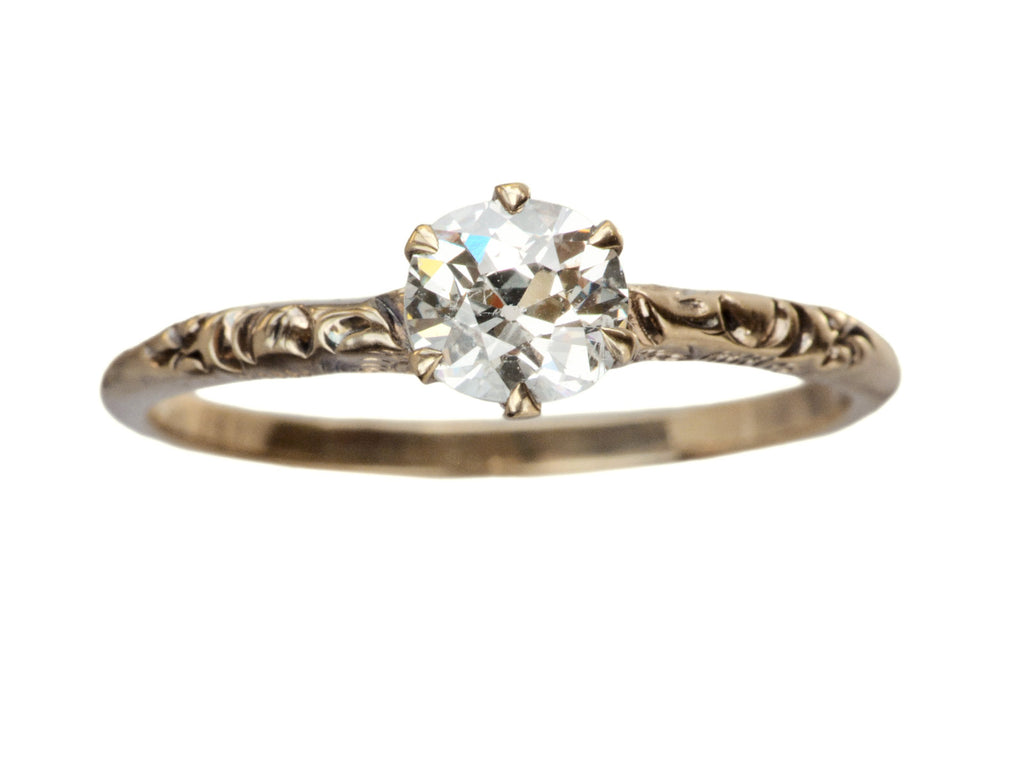 Victorian solitaire with a slightly oval shaped diamond set in a pattered slender rose gold mounting, shown on white background.
