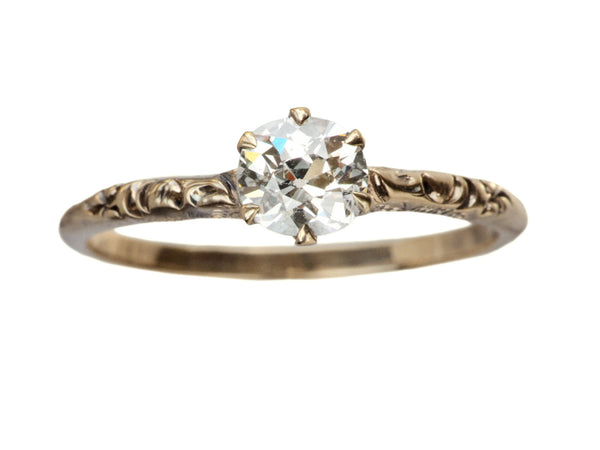 Victorian solitaire with a slightly oval shaped diamond set in a pattered slender rose gold mounting, shown on white background.