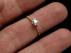 thumbnail of Victorian solitaire with a slightly oval shaped diamond set in a pattered slender rose gold mounting, shown on finger.