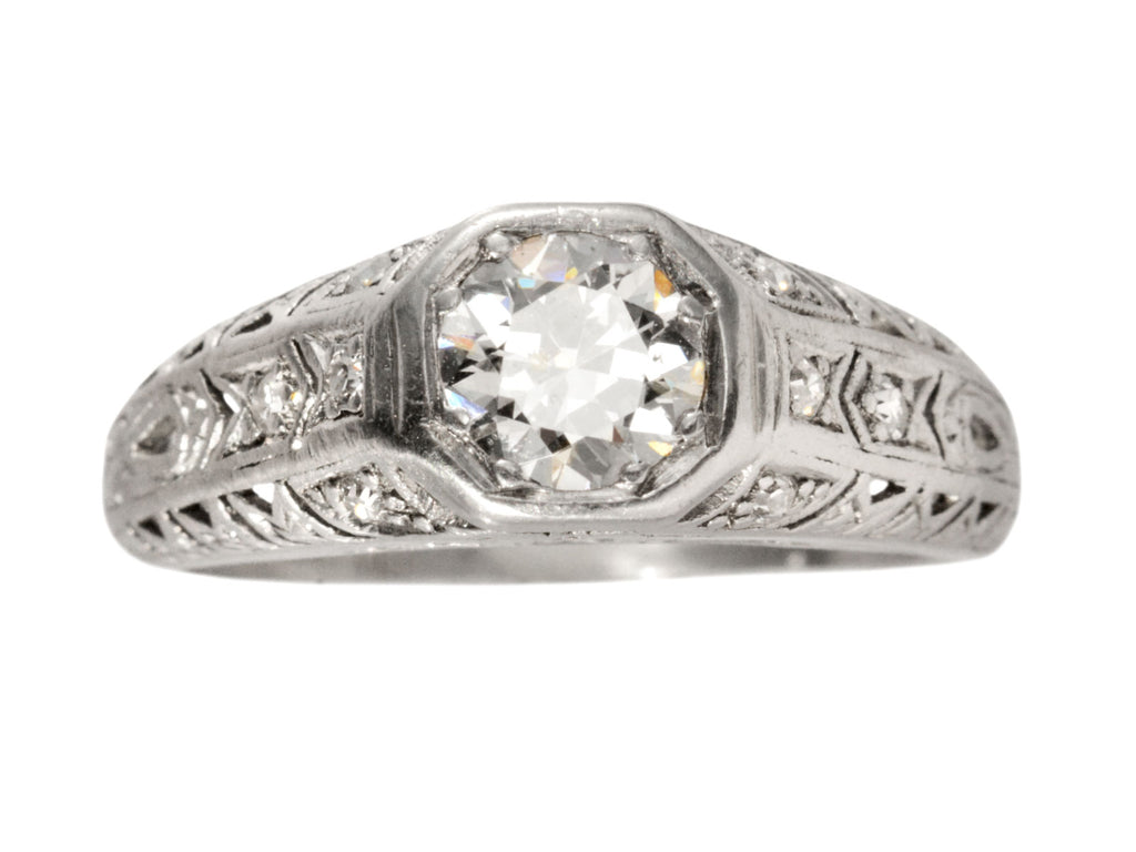 A c1920 Art Deco engagement ring with a round white diamond in a wide filigreed platinum mounting (shown on white background)