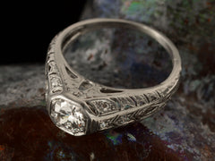 thumbnail of Angled top view of a c1920 Art Deco engagement ring with a round white diamond in a wide filigreed platinum mounting (shown on dark textured background)