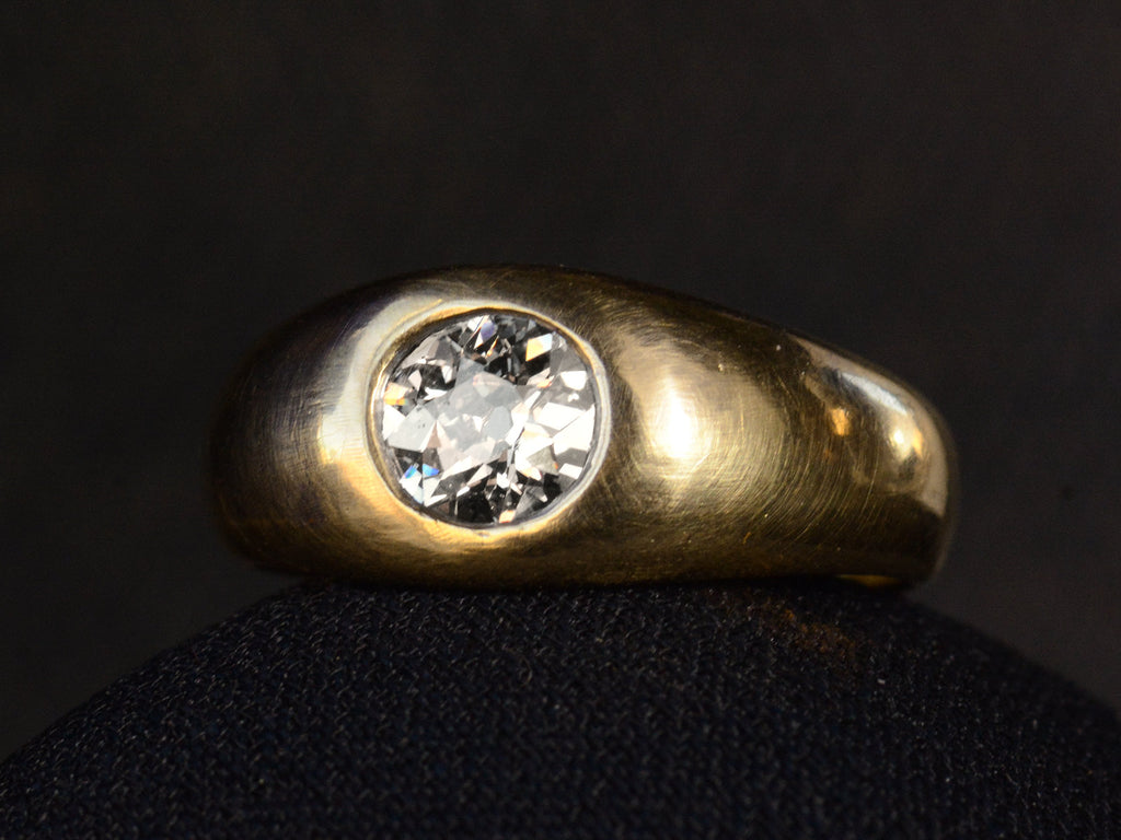 Right angled view of a wide rounded antique yellow gold ring with a flush-set old European cut diamond, shown on dark background.