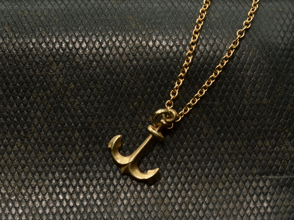 Gold anchor necklace on a textured black background

