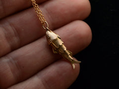 thumbnail of Gold fish-shaped pendant on a chain held between fingers against a dark background