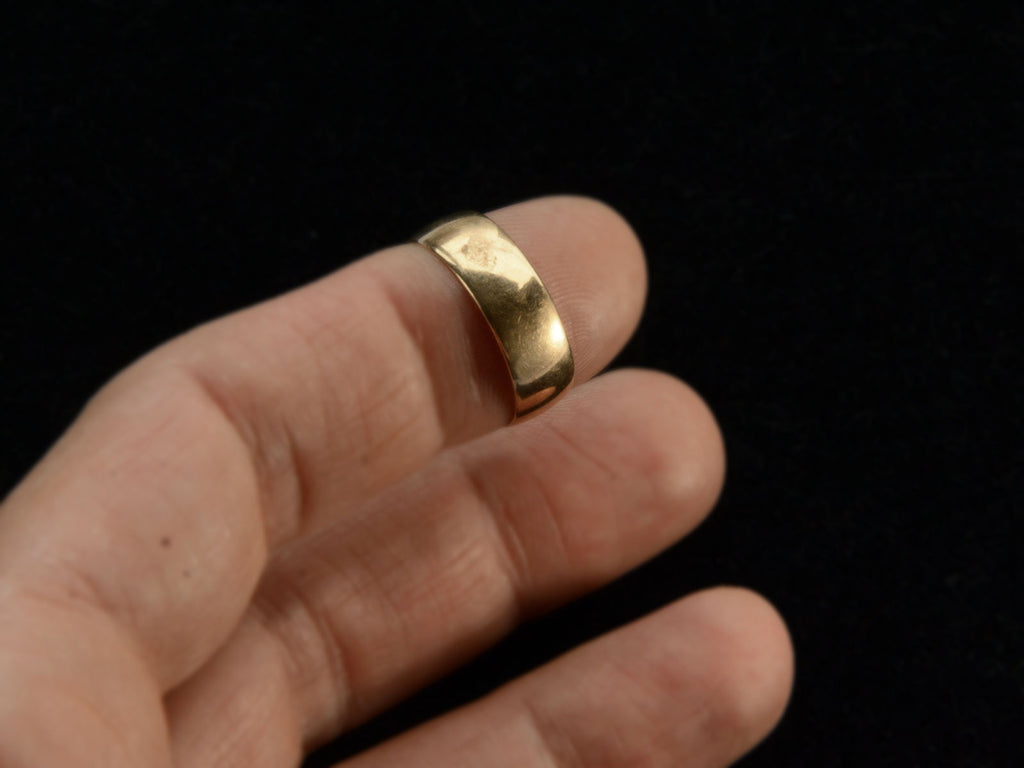 A wide Victorian wedding band in a rosy-yellow gold, shown on a finger.