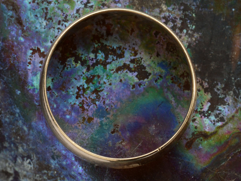 The side profile of a  wide Victorian wedding band in a rosy-yellow gold, shown on colorful background.