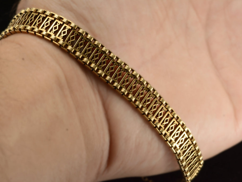 A c1880 French 18K yellow gold bracelet with filigreed links, shown stretched over hand