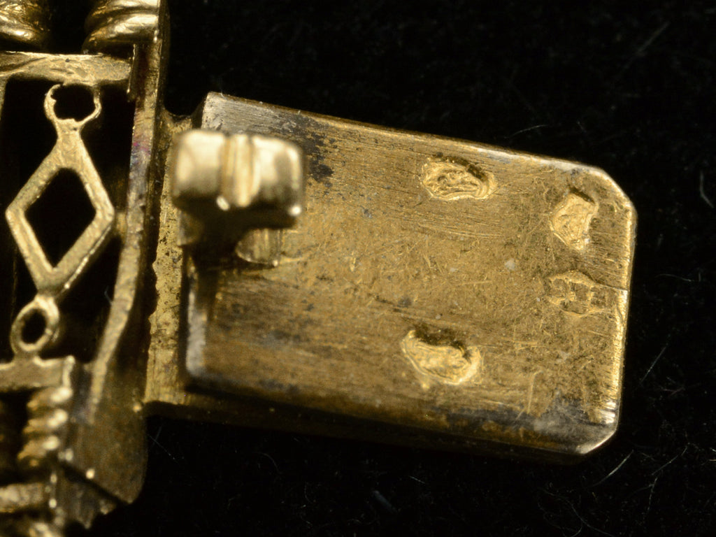 Close up of gold clasp tongue showing French hallmarks: two eagle head punches, an unclear animal head, and a maker's mark possibly having the letters E and C.