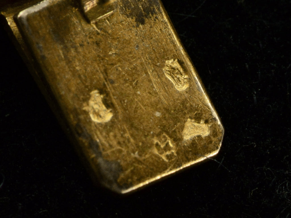 Alternate focus close up of gold clasp tongue showing French hallmarks: two eagle head punches, an unclear animal head, and a maker's mark possibly having the letters E and C.