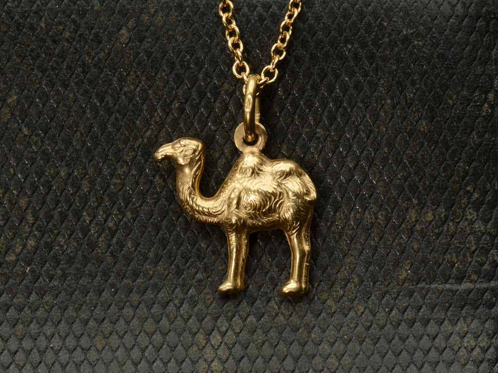 A c1960 18K yellow gold Camel Charm on a cable chain. A stamp on the bale reads "750" On dark textured background.