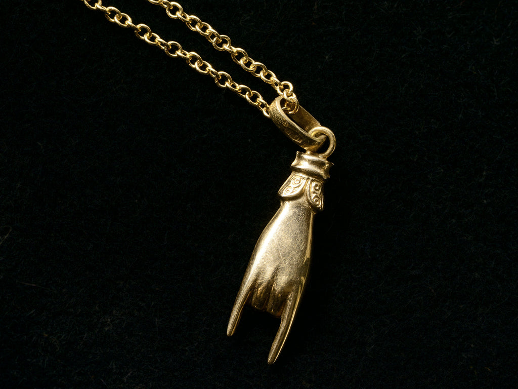 Back of a vintage gold hand charm on a chain, gesturing the sign of the horns, shown on black background.