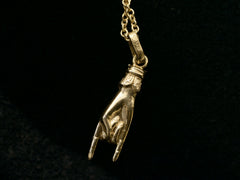 thumbnail of A vintage gold hand charm on a chain, gesturing the sign of the horns, shown on black background. "750" stamp visible on bale