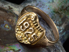 thumbnail of Angled view of Art Deco yellow gold signet ring with the year "1925" on a shield shaped signet face. Shown on dark background.