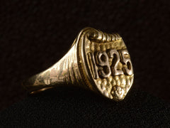 thumbnail of Left side view of Art Deco yellow gold signet ring with the year "1925" on a shield shaped signet face. Shown on dark background.