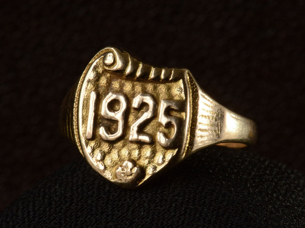 Right front view of Art Deco yellow gold signet ring with the year "1925" on a shield shaped signet face. Shown on dark background.
