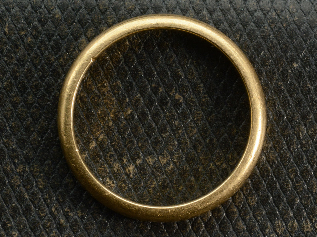 Side profile of a rounded 18K yellow gold wedding band shown on textured dark background.