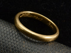 thumbnail of Angled view of a rounded 18K yellow gold wedding band shown on dark background. Inscription inside ring is visible: "Hans 34"