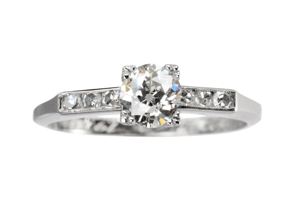 A simple Art Deco platinum engagement ring with a round old cut diamond in four prongs between 3 smaller diamonds on each side, shown on white background.