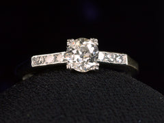 thumbnail of Front view of a simple Art Deco platinum engagement ring with a round old cut diamond in four prongs between 3 smaller diamonds on each side, shown on dark background.